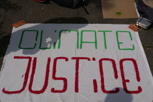 Weißes Banner mit "Klimagerechtigkeit" darauf, vor Karton, einer Tüte und anderen Gegenständen auf dem Boden