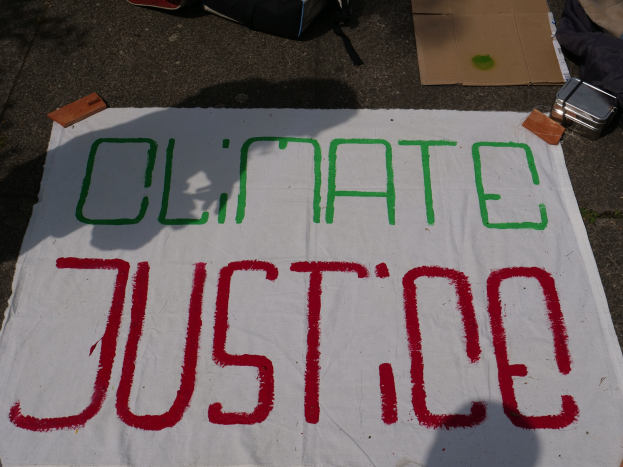 Weißes Banner mit "Klimagerechtigkeit" darauf, vor Karton, einer Tüte und anderen Gegenständen auf dem Boden