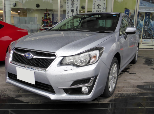 Silberner Wagen vor einem roten Wagen geparkt, mit einer Glaswand im Hintergrund, die einen Weihnachtsbaum, Lichter und andere Gegenstände sowie Plakate mit Text und Bildern von Autos zeigt.