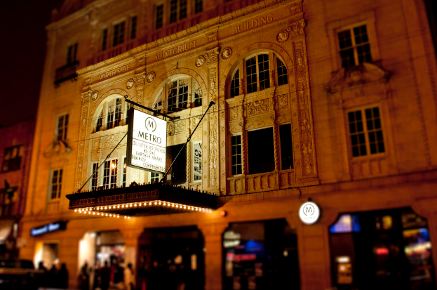 Ein gelbes Geb├Ąude mit Gesch├Ąften unten, von denen eine ein wei├čes Schild mit der Aufschrift 'Metro' hat.
