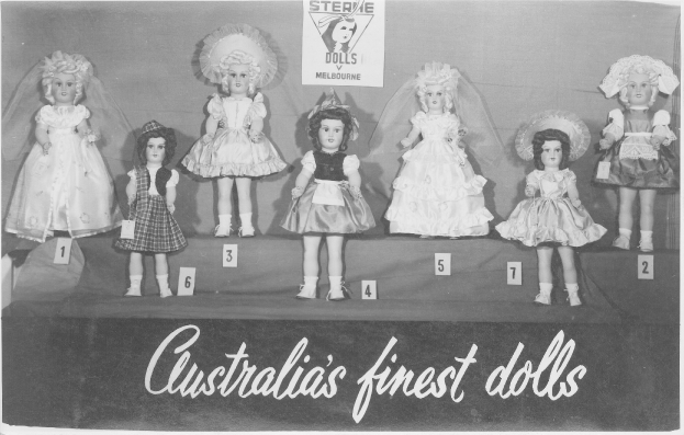 Ein Schwarz-Weiß-Foto einer Reihe australischer Puppen, jede mit einzigartigen Outfits und Frisuren, vor einem Plakat mit Text und Logo.