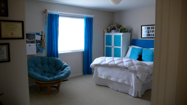 Ein Raum mit einem Bett, einem Stuhl, einem Fenster mit Vorhängen, einem Schrank, einem Foto Rahmen und einem gefliesten Boden.