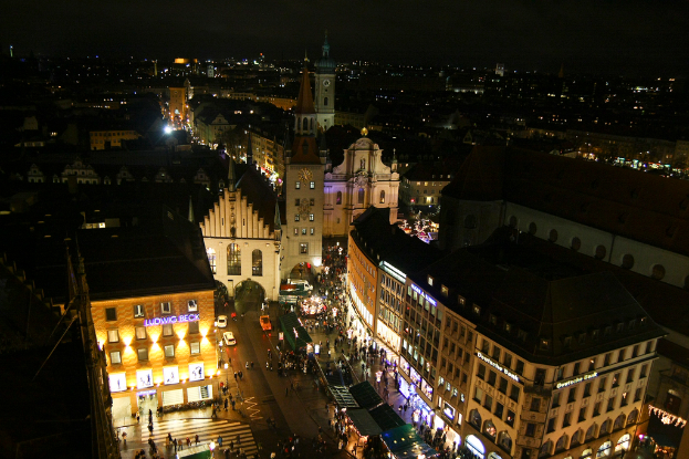 Eine Vogelperspektive auf eine nächtliche Stadt mit zahlreichen Gebäuden, Häusern, Straßen voller Fahrzeuge und Menschen.