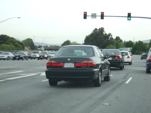 Eine belebte Straße mit mehreren Fahrzeugen, drei Strommasten und einem Verkehrsschild auf der rechten Seite unter einem klaren Himmel.