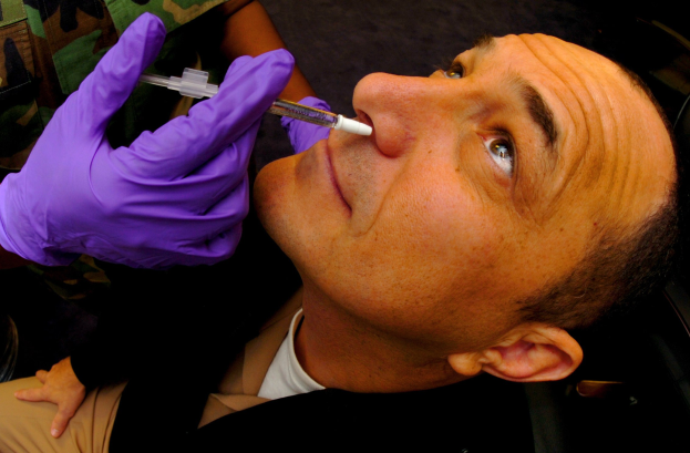 Ein Arzt in lila Handschuhen injiziert ein Vakzin in den Mund eines Mannes mit einer Spritze.