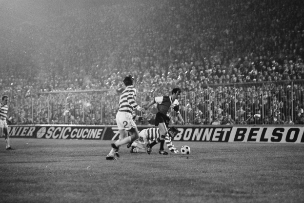 Ein Schwarz-Weiß-Bild einer Gruppe von Männern, die auf einem Feld Fußball spielen, mit Zuschauern auf den Tribünen und einer Fahne mit der Aufschrift "Celtic v West Bromwich Albion - FA Cup Third Round."