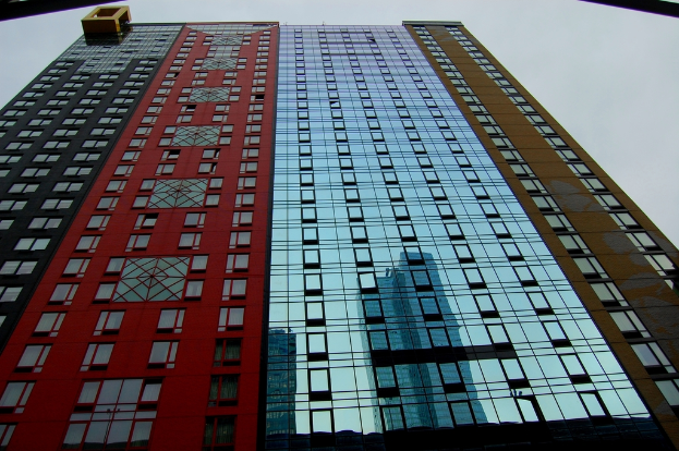 Ein hohes Gebäude mit Fenstern, die andere Gebäude und einen bewölkten Himmel reflektieren.