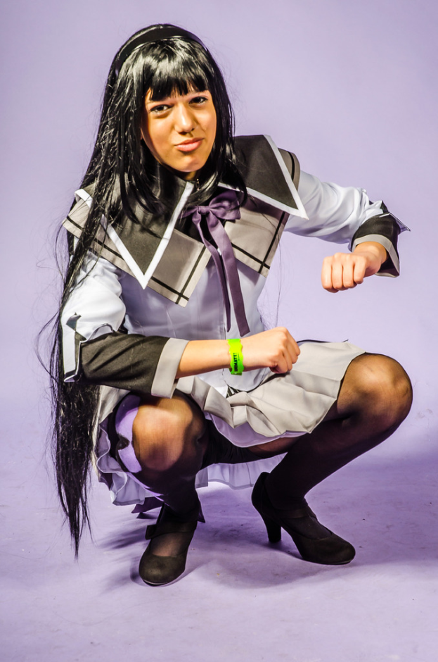 Eine Person in einem Kostüm lächelt, während sie auf einem violetten Hintergrund hockt.