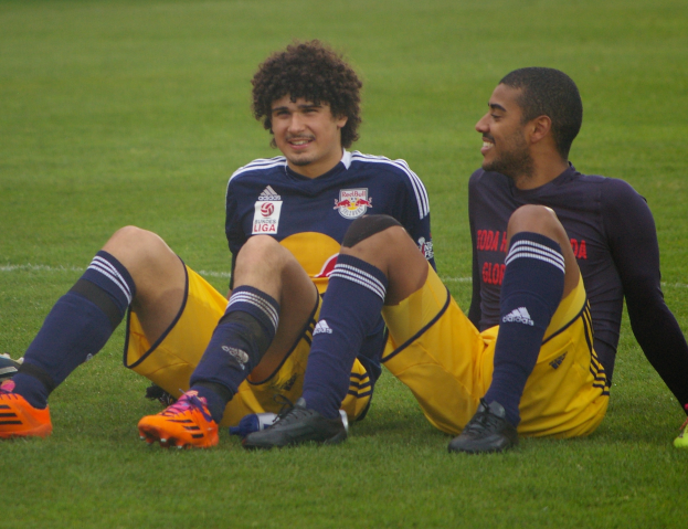 Zwei Fussballspieler sitzen auf dem Boden mit Überkreuzten Beinen, tragen Sportkleidung und löchen sich an.