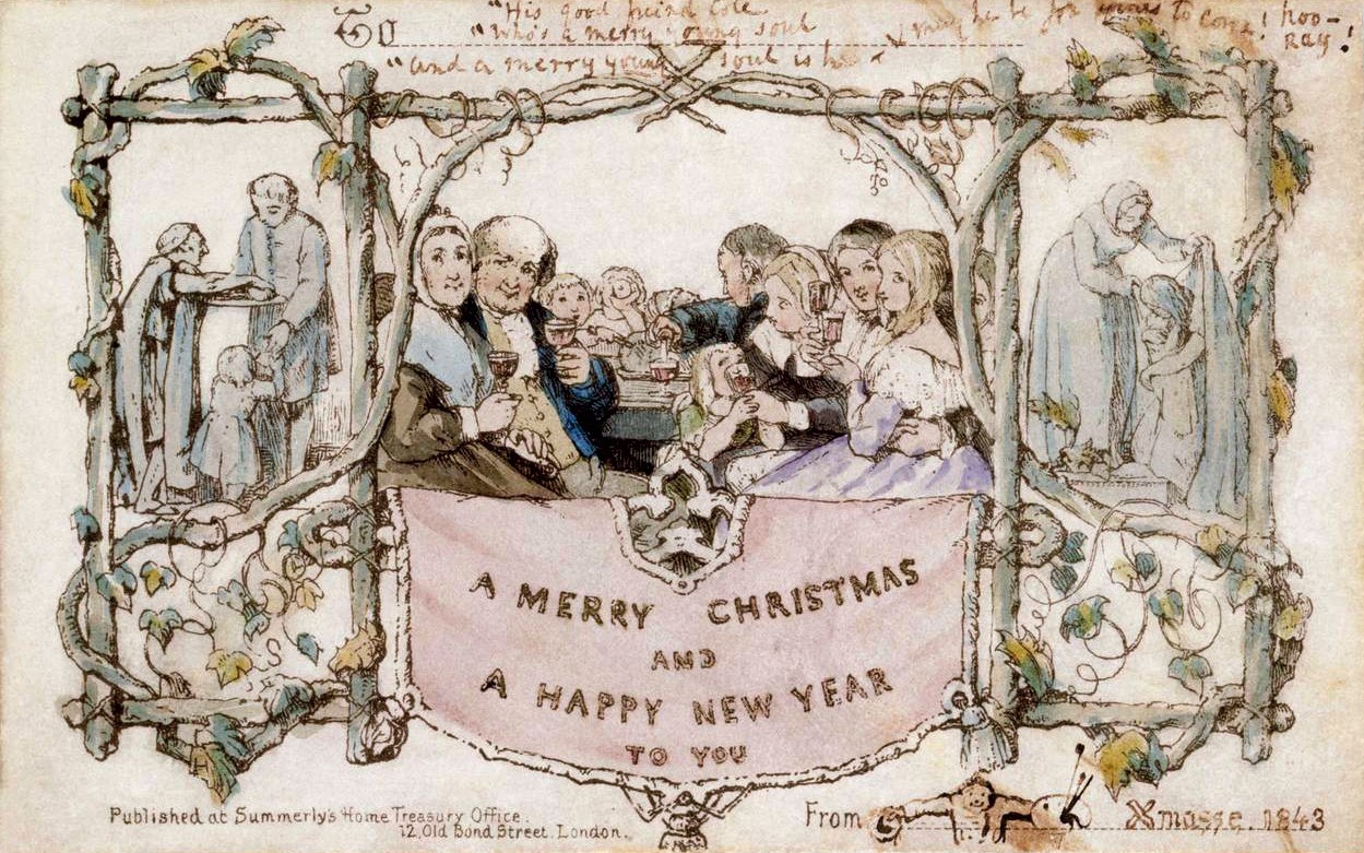 Eine Gruppe von Menschen in Festkleidung versammelt sich um einen Tisch unter einem Banner mit der Aufschrift "Fröhliche Weihnachten und ein gutes neues Jahr", die während einer Feier lachen.