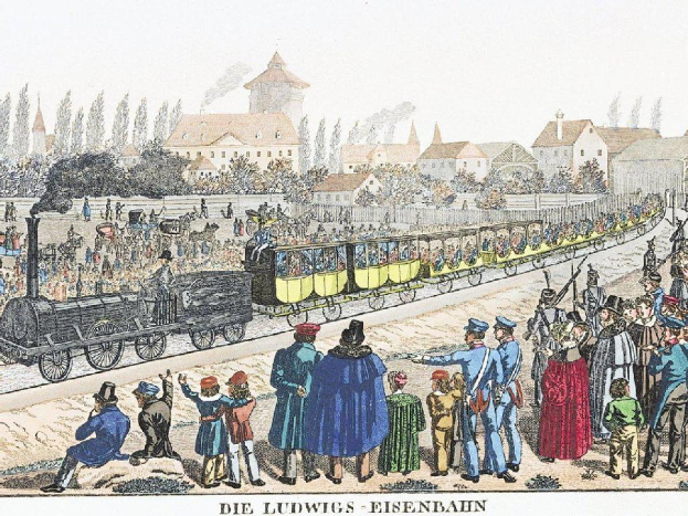 Eine Gruppe von Menschen steht um einen Zug auf einem Gleis, mit einigen Passagieren im Zug und anderen außerhalb, vor Gebäuden und Bäumen im Hintergrund, mit der Bildunterschrift "Ludwigs-Eisenbahn, der erste Bahnhof in Deutschland" unten.