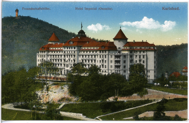 Alte Ansichtskarte des Hotel Imperial in Karlsbad, Deutschland, zeigt ein großes Gebäude mit Fenstern, umgeben von Bäumen, Pflanzen, Gras, einem Pfad, einer Baumgruppe, Hügeln und einem bewölkten Himmel, mit Text oben.