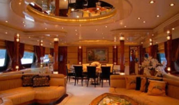 Ein Hotellobby mit Sofas, Stühlen, Tischen und Dekorationsgegenständen im Vordergrund, Fenstern mit Vorhängen und Lampen auf beiden Seiten, einem gerahmten Bild und Beleuchtung im Hintergrund und einem Spiegel mit Deckenbeleuchtung oben.