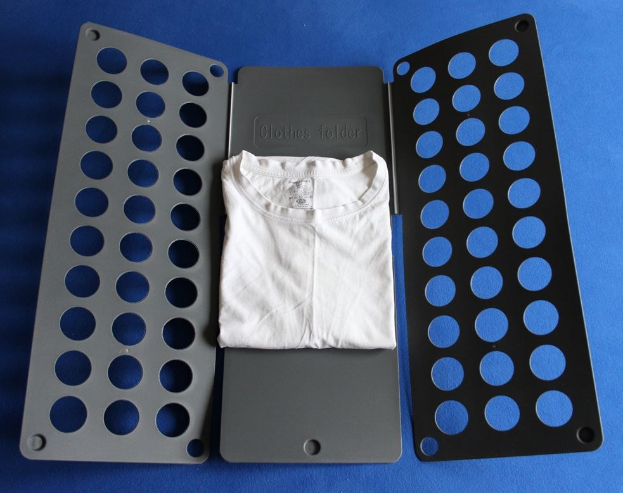 Ein weißes T-Shirt auf einer blauen Oberfläche neben einem schwarzen und aschfarbenen Kleiderordner mit Löchern.