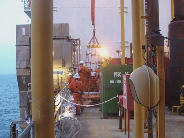 Ein Schiff mit Masten, Kisten und Gel├Ąndern, mit Menschen in Helmen und Wasser im Hintergrund.