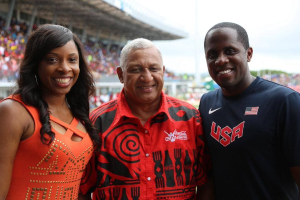 Drei Personen, die vor einem Stadion mit Zuschauern und Himmel im Hintergrund lächeln, mit einem Coca-Cola Games 2014-Wasserzeichen.