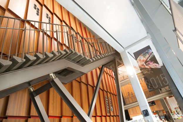 Eine Metalltreppe mit einem Metallstab-Geländer, Säulen, Bannern und Metallzäunen auf den Fluren, mit einigen Objekten auf Regalen im Hintergrund.