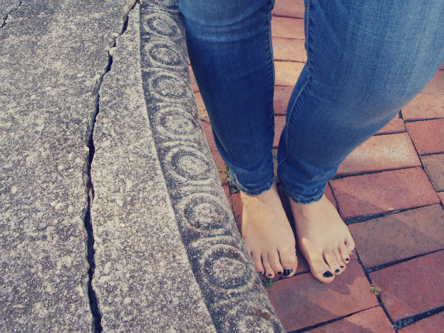 Eine gebrochene Wand auf der linken Seite und zwei Beine einer Person auf einem Fußweg auf der rechten Seite.