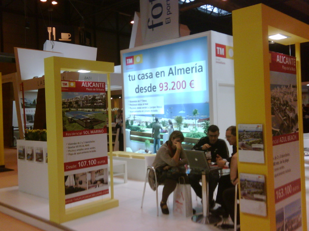 Eine Gruppe von Menschen, die um einen Tisch herum auf Stühlen sitzen und auf einen Laptop schauen, mit mehreren Flyern mit verschiedenen Werbeanzeigen daneben.