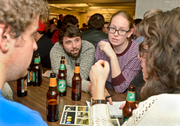 Mehrere Personen stehen auf beiden Seiten eines Tisches mit Bierflaschen in einer Art Bar.