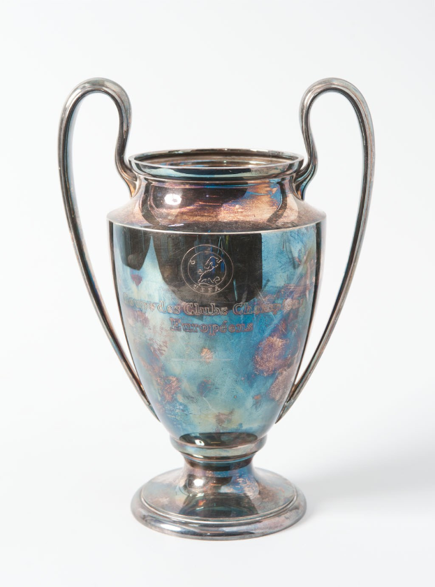 Der UEFA-Champions-League-Pokal, ein Stahlbecher mit zwei Griffen und einem blauen und silbernen Farbschema, der mit 'UEFA Champions League' beschriftet ist, vor einem weißen Hintergrund dargestellt.