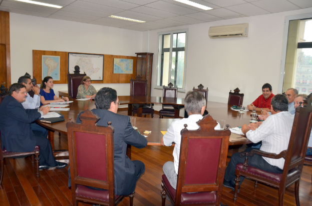 Eine Gruppe von Menschen, die an einem Tisch sitzen und Papiere und Gläser vor sich haben, im Hintergrund ein Klimagerät, eine Anschlagtafel und Karten an der Wand