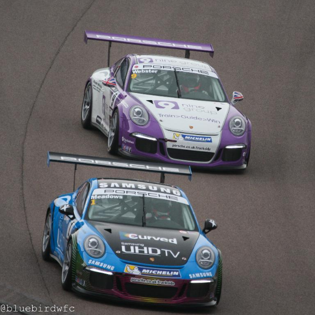 Zwei Autos auf einer Straße vor einer Stadt, mit Text in der linken unteren Ecke.