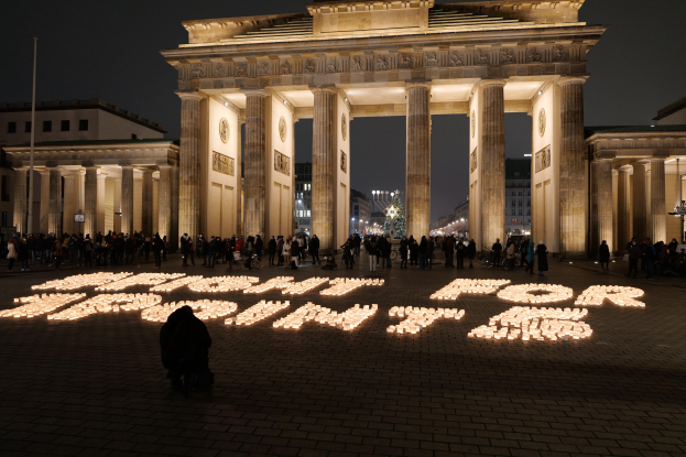 Eine Gruppe von Menschen steht vor dem beleuchteten Reichstagsgebäude in Berlin, Deutschland, umgeben von Gebäuden, Pfählen und Lichtern; die Wörter "Kampf für Freiheit" sind im Vordergrund zu sehen.