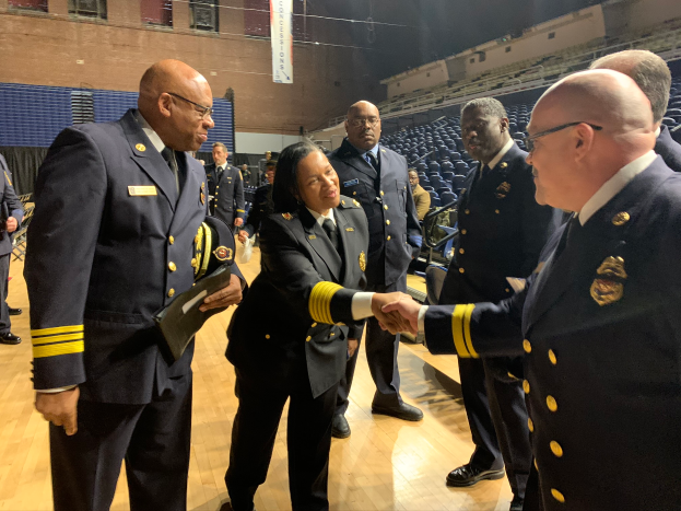 Eine Gruppe von Menschen in Uniform schüttelt sich vor einer Menge die Hand, im Hintergrund ein Banner mit der Aufschrift "Feuerwehrchef und Beamter des Jahres".