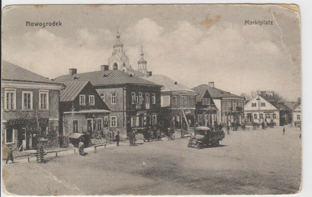 Ein altes Schwarz-Weiß-Foto einer Stadtstraße in Nowogrodeek, Deutschland, das Gebäude, Menschen, Karren, Pfähle, Bäume und Himmel zeigt, mit der Aufschrift "Marktplatz in Nowogrodeek, Deutschland" oben und unten.