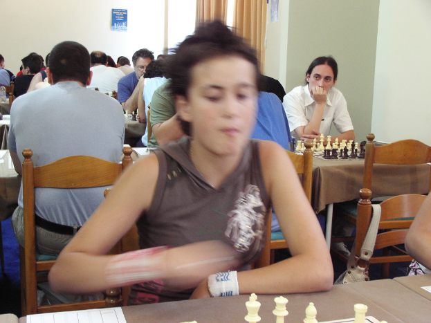 Ein Raum mit Menschen an Tischen beim Schachspielen, einer Vorhangwand und einem Foto in der Ecke.