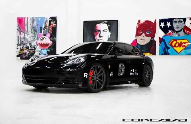 Ein schwarzer Nissan-Sportwagen ist mit Cartoon-Plakaten im Hintergrund und einer kleinen Inschrift am unteren Bildrand zu sehen.