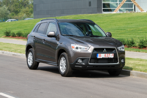 Ein braunes Auto, das auf der Seite einer Straße mit Grünfläche und einem Glaswandhaus im Hintergrund geparkt ist, mit zwei weiteren Autos an der Ecke.