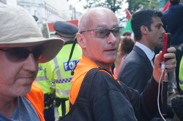 Eine Gruppe von Menschen, die mit einer Person mit Mütze auf der linken Seite und einem Polizisten im Hintergrund steht.