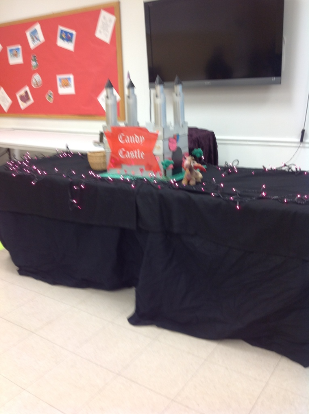 Ein Raum mit zwei schwarz gedeckten Tischen, die Burgzinnen zeigen, ein rotes Whiteboard mit Fotos und einen Fernseher.