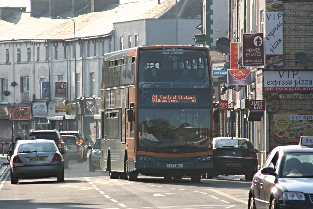 Eine Straße mit Autos und einem Bus vor Gebäuden mit Wänden, Fenstern, Tellern und Dächern, mit Plakaten und Bannern an den Wänden und einem Pfahl mit einer Straßenlaterne.