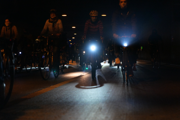 Gruppe von Menschen, die nachts auf beleuchteter Stadtstraße Fahrräder fahren, alle mit Helmen