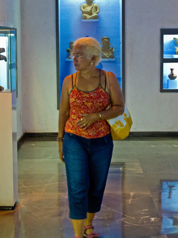 Eine Frau mit einer Handtasche steht vor einer Wand mit Fotorahmen und Statuen.