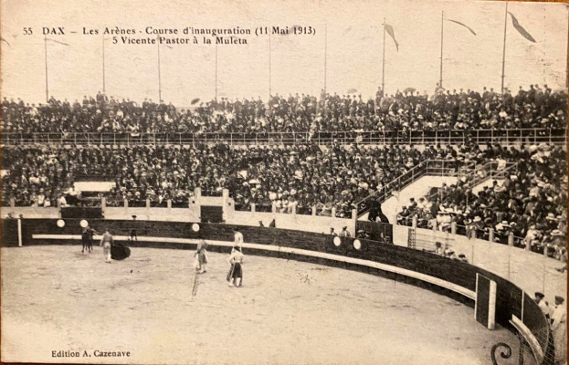 Schwarzes und weißes Foto eines Boxkampfes in einem Stadion mit Zuschauern auf den Rängen und einer Gruppe von Menschen in der Mitte.