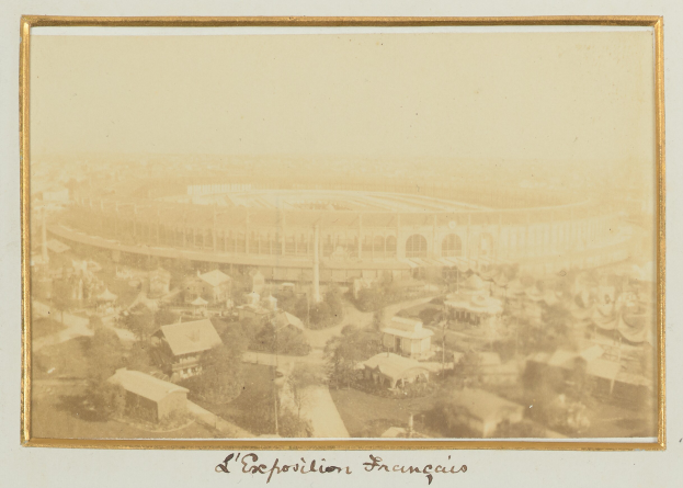 Altes Schwarz-Weiß-Foto eines Stadions, umgeben von Gebäuden, Bäumen und Strommasten mit Text unten.