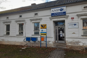 Weißes Gebäude mit der Aufschrift "Anipol Post Office", Fenstern, Tür, Weg, Gras, Baum, Pfosten und bewölktem Himmel.
