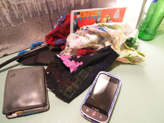 Tuchstücke, ein Mobiltelefon und eine Geldbörse sind auf einer Oberfläche angeordnet.