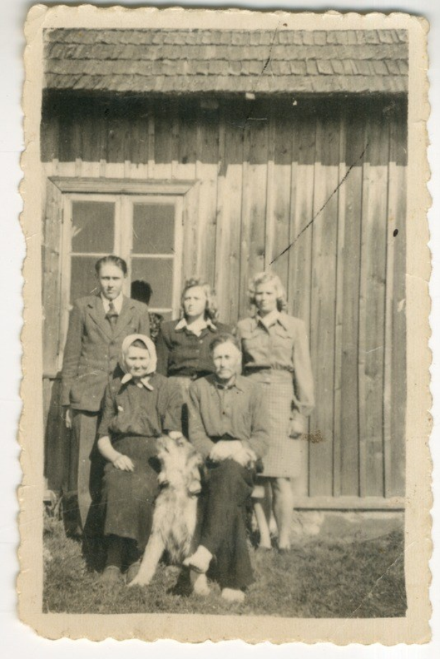 Schwarzes und weißes Foto einer Familie mit einem Hund vor einem Haus mit einem Fenster.