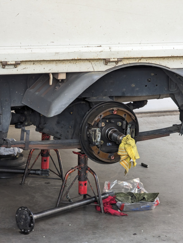 Ein gelbes Tuch liegt über einem Lastwagen, der in einer Garage geparkt ist, mit verstreuten Werkzeugen und Gegenständen davor.