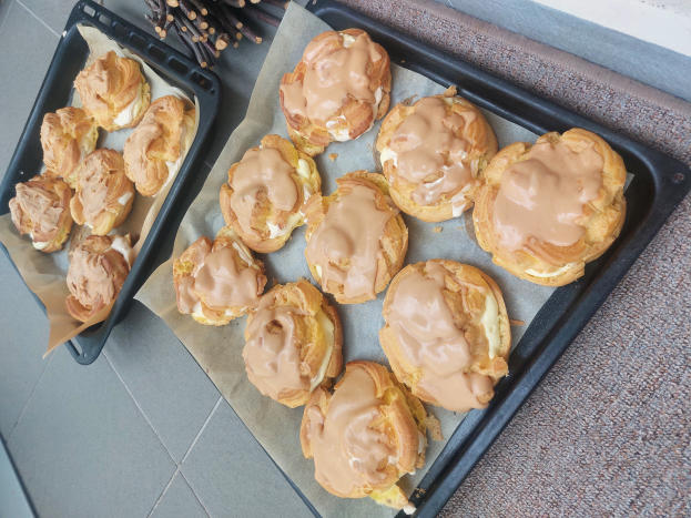Ein Tablett voller gemischter dänischer Keks mit einem hellen goldbraunen Farbton und einer fluffigen Textur, einige mit Puderzucker bestäubt, liegt auf einer Theke neben einem offenen Fenster, gebadet in warmem Licht.