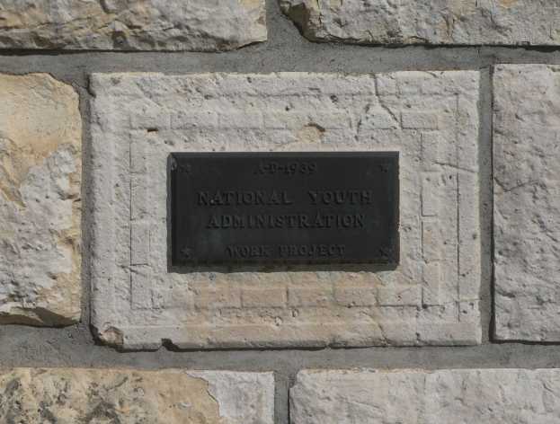 Eine Steinwand mit einem rechteckigen Schild, auf dem in fetter, weißer, zentrierter Schrift 'Nationaler Jugendausschuss' steht, auf einem schwarzen Hintergrund.