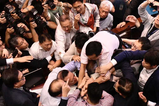 Eine Gruppe von Menschen steht zusammen vor einer Menge, einige halten Kameras, im Hintergrund sind Tische mit Papieren und anderen Gegenständen zu sehen, was auf eine hitzige Diskussion im Zusammenhang mit der Hongkonger Börsenschließung aufgrund der Coronavirus-Pandemie hindeutet.