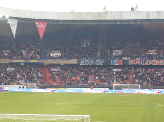 Ein Rasenplatz mit Torpfosten auf beiden Seiten, Zuschauern im Hintergrund und zahlreichen Werbetafeln in der Mitte und darüber.