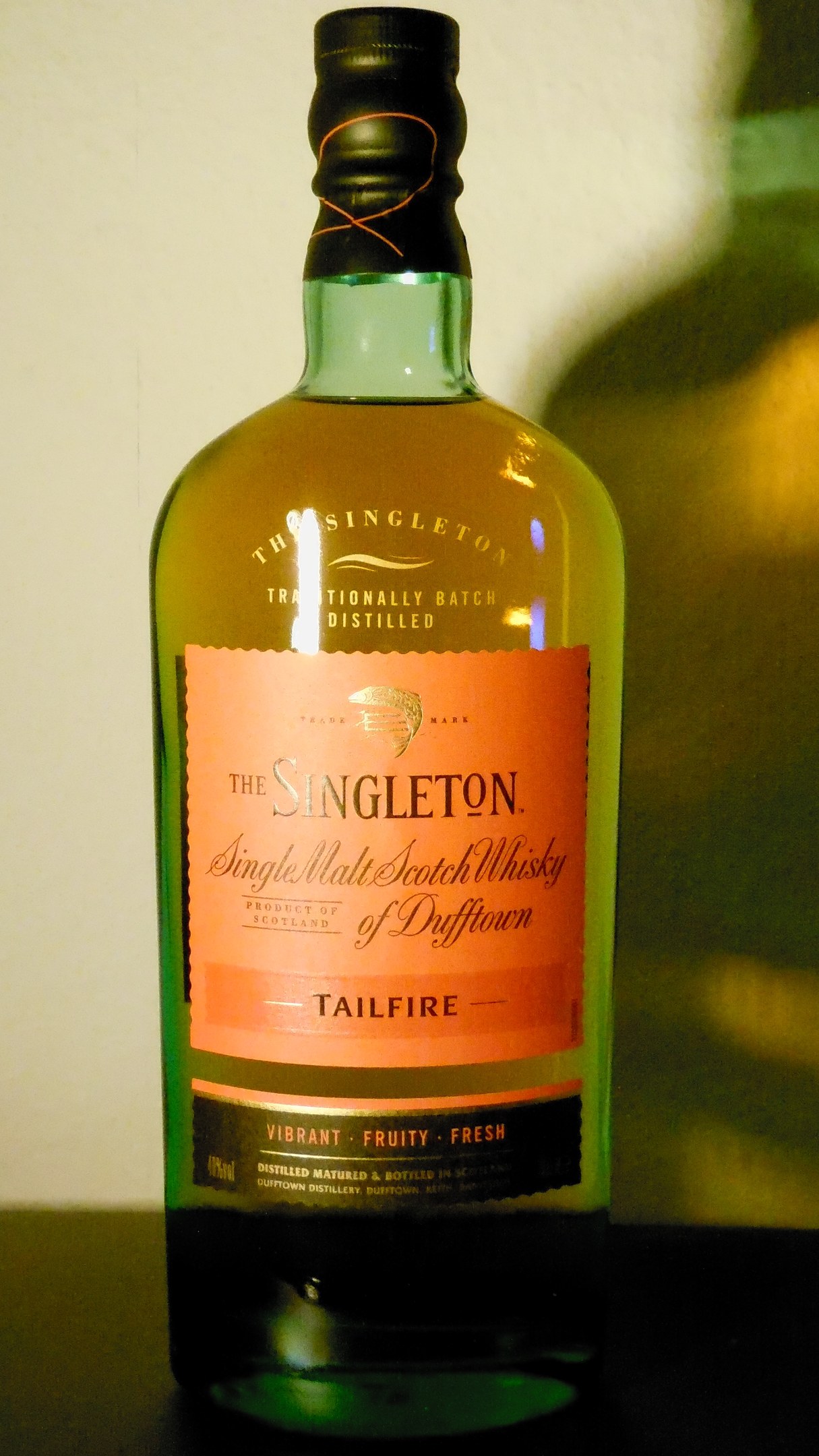 Eine tiefe bernsteinfarbene Flasche Singleton of Dufftown Tailfire Single Malt Scotch Whisky mit einem schwarzen Etikett, das eine schlichte Schrift und ein Wappen mit einem Löwen und einer Burg zeigt.