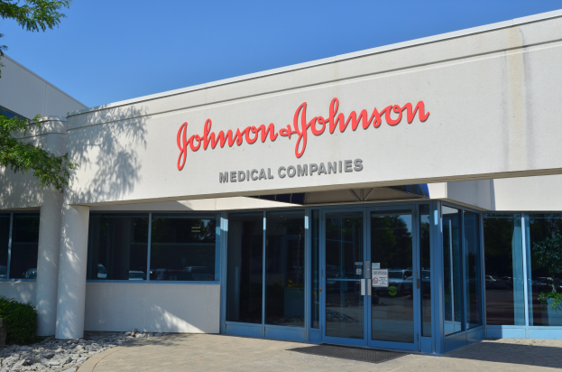 Außenansicht des Johnson & Johnson Medical Companies-Gebäudes mit Glaswänden und -türen, lesbarer Text an der Wand, Landschaftssteinen, Pflanzen und einem Baum auf der linken Seite, unter einem klaren blauen Himmel.